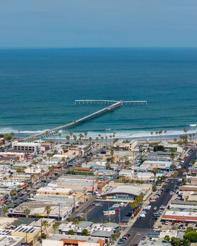 Aerial view of coastal residential neighborhood with Pacific Ocean, sandy beach, and distant bay under blue sky